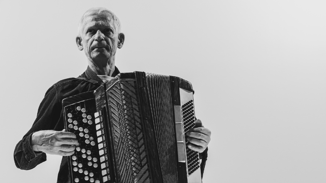 Ein alter Mann, der mit Hoffnung in den Augen ein Akkordion spielt
